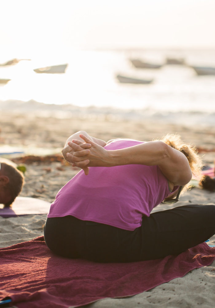 Women doing yoga exercises or supported pigeon pose on an empty beach of the Indian ocean in Mauritius