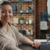 Software engineer typing source code on computer keyboard turning head and smiling at camera. Casual database admin computing big data in it startup company feeling confident.